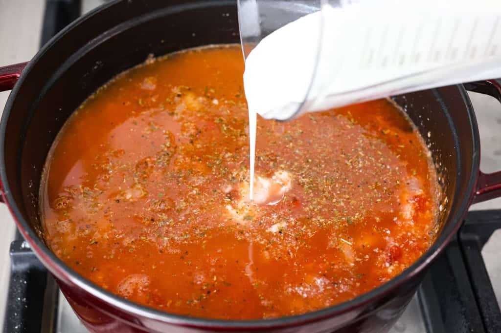 Creamy Tuscan garlic tortellini soup is so easy to make and one of the best soups that you will make! This soup is loaded with cheesy tortellini, diced tomatoes healthy spinach and hearty white beans. This soup is so creamy and delicious, I know your family will love it! Overhead shot of heavy cream being poured in to the soup.