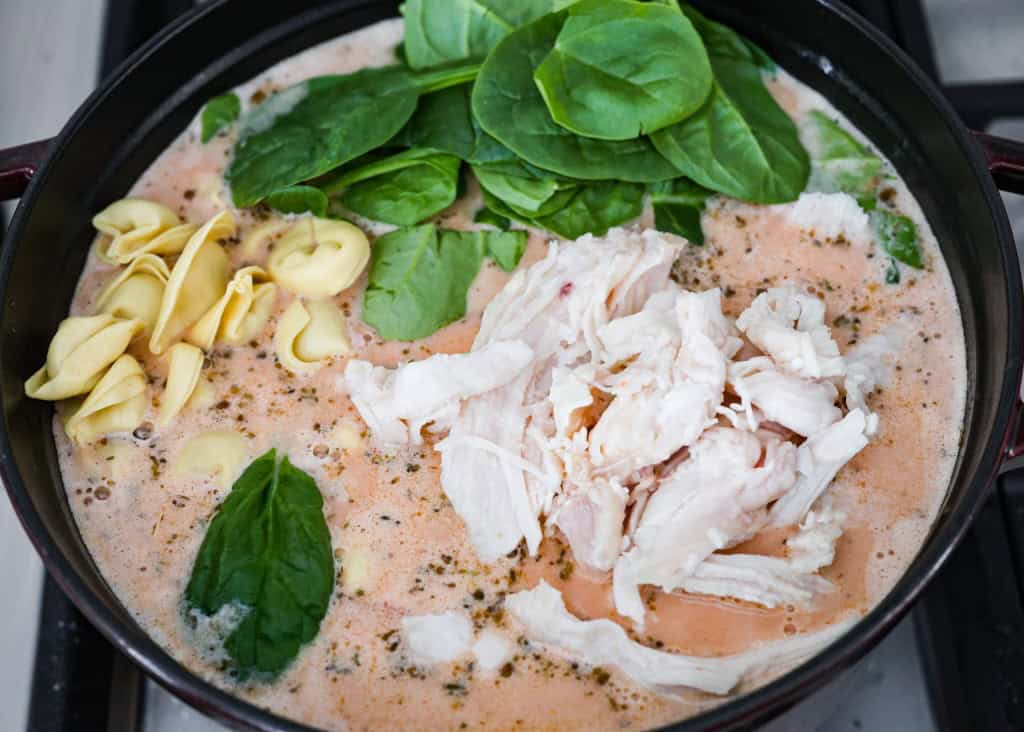 Creamy Tuscan garlic tortellini soup is so easy to make and one of the best soups that you will make! This soup is loaded with cheesy tortellini, diced tomatoes healthy spinach and hearty white beans. This soup is so creamy and delicious, I know your family will love it! Overhead shot of the soup mix with heavy cream with added chicken spinach and tortellini.