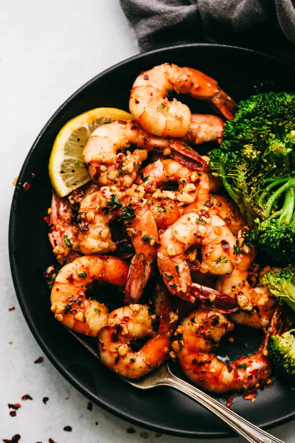 Brown Butter Spicy Garlic Shrimp is an incredibly easy meal that is ready in under 10 minutes! The brown butter flavor is so luxurious over the spicy garlic shrimp. It will wow your family! Brown Butter Spicy Garlic Shrimp on a black plate with broccoli.