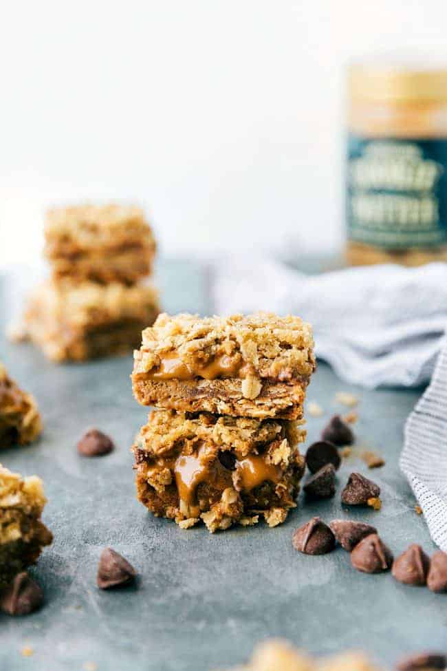 Biscoff Oatmeal Bars are easy to make oatmeal bars with a thick layer of biscoff and milk chocolate! Biscoff oatmeal bar stacked on top of each other up with chocolate chips surrounding them on the table