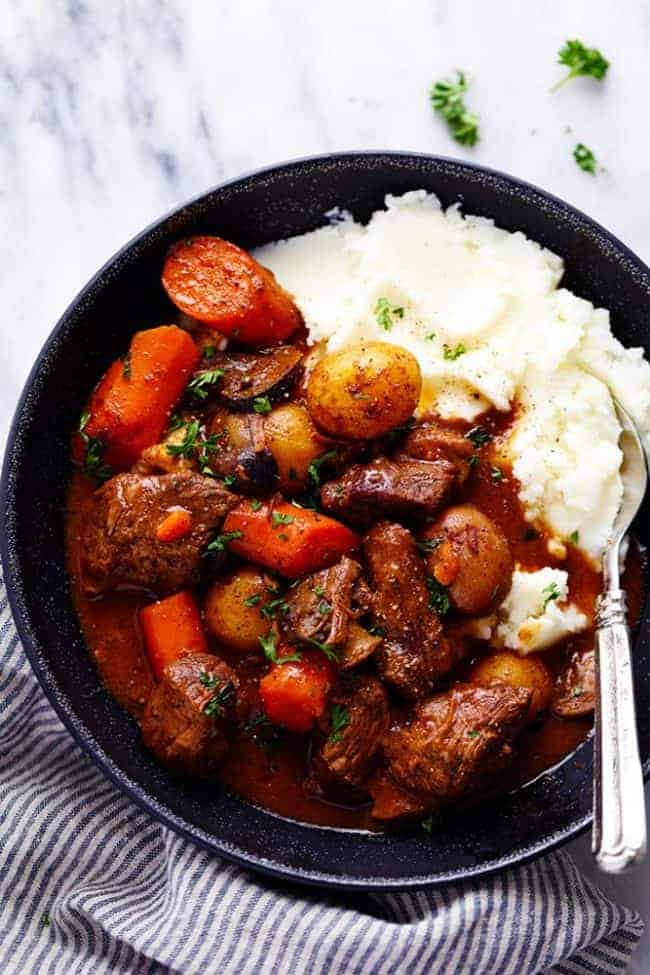 Slow Cooker Beef Bourguignon has crazy tender melt in your mouth beef and hearty veggies slow cooked to perfection in a rich sauce. ย This meal is comforting and perfect for the cold months ahead! slow Cooker Beef Bourguignon with mashed potatoes on a plate