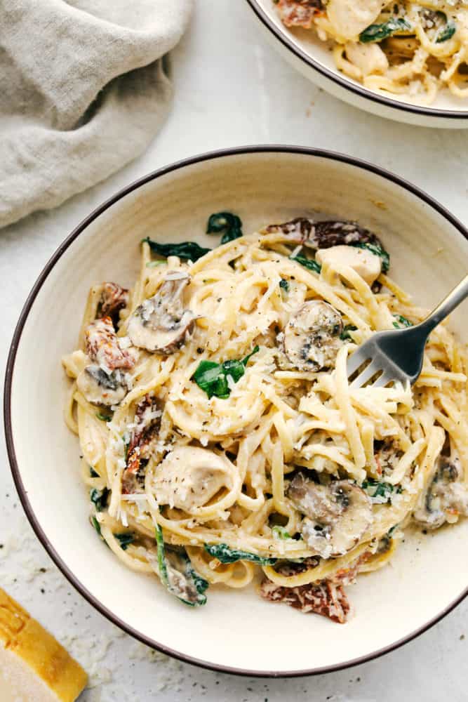 One Pot Creamy Chicken Mushroom Florentine is ready in under 30 minutes! Everything is made in just one pot and it is filled with sun dried tomatoes, spinach, mushrooms and the creamiest pasta! One pot creamy chicken mushroom Florentine in a bowl with a fork in it.
