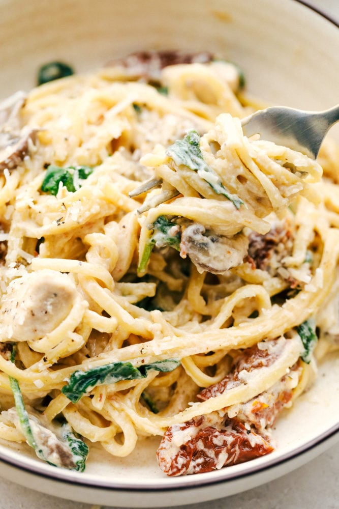 One Pot Creamy Chicken Mushroom Florentine is ready in under 30 minutes! Everything is made in just one pot and it is filled with sun dried tomatoes, spinach, mushrooms and the creamiest pasta! A bowl full of chicken mushroom Florentine with a fork.