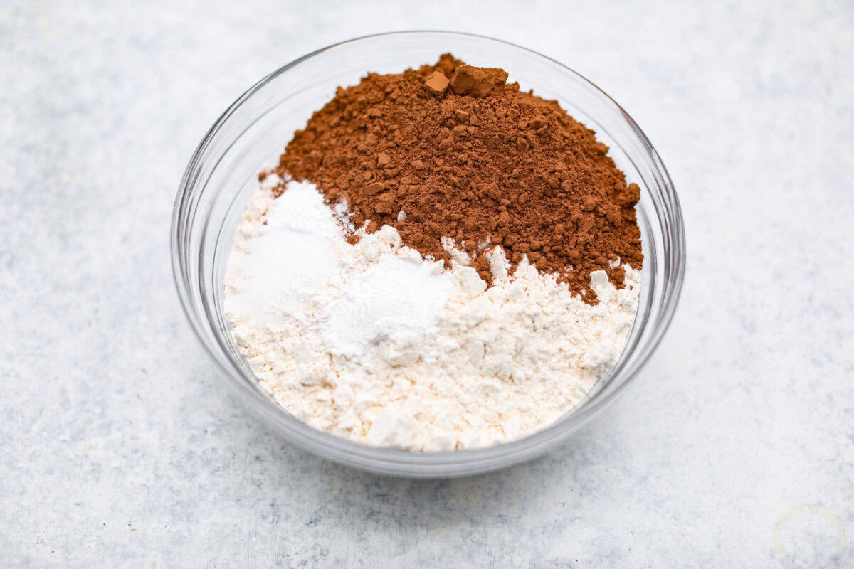 Chocolate Snowball Cookies are tender chocolate cookies with the best texture! A buttery cookie made with cocoa powder and ground walnuts gets coated in sweet powdered sugar. Make this classic holiday cookie a tradition every year! Fourth photo of the flour ingredients added to a bowl.