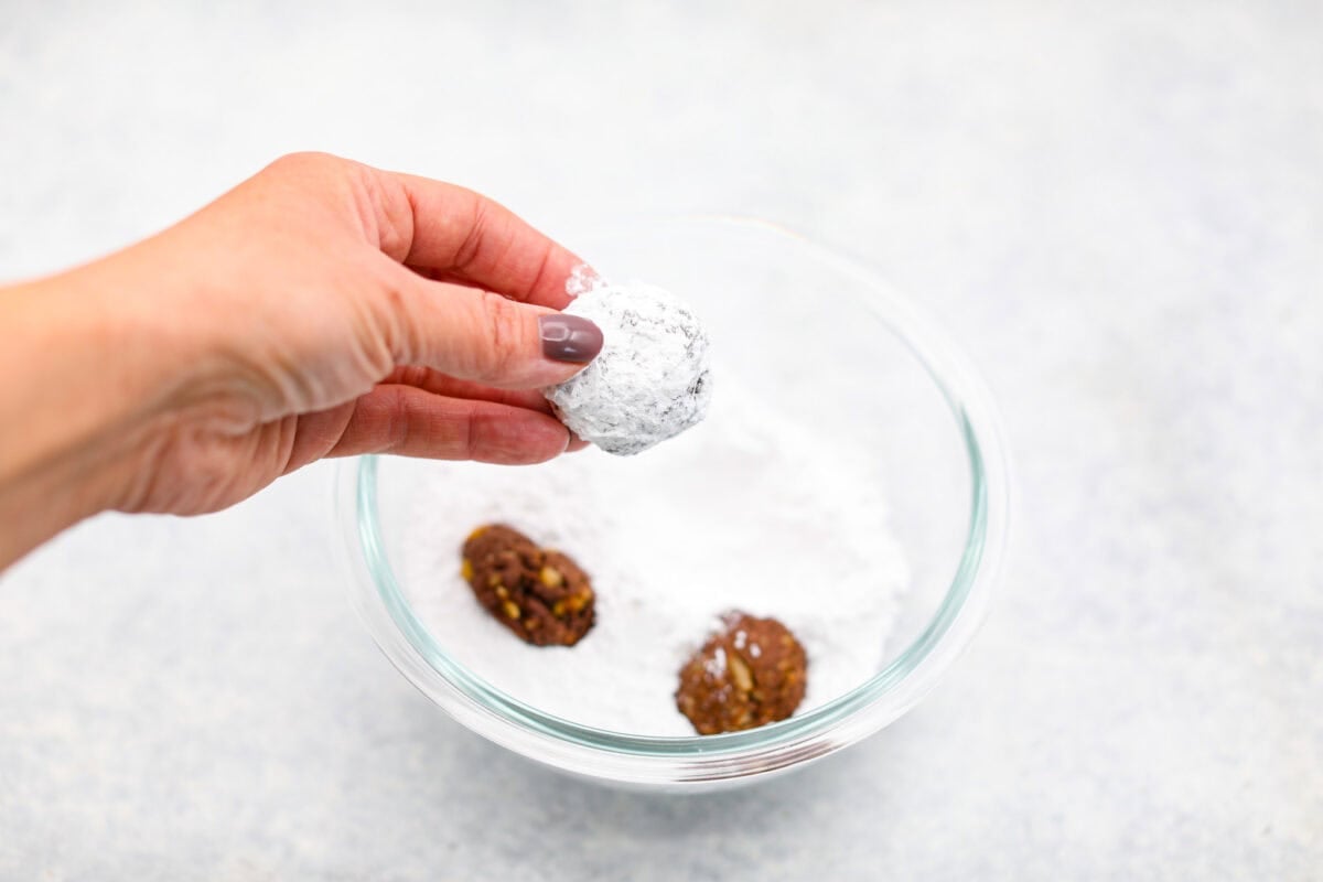 Chocolate Snowball Cookies are tender chocolate cookies with the best texture! A buttery cookie made with cocoa powder and ground walnuts gets coated in sweet powdered sugar. Make this classic holiday cookie a tradition every year! Seventh photo of the baked cookies dipped in powdered sugar.