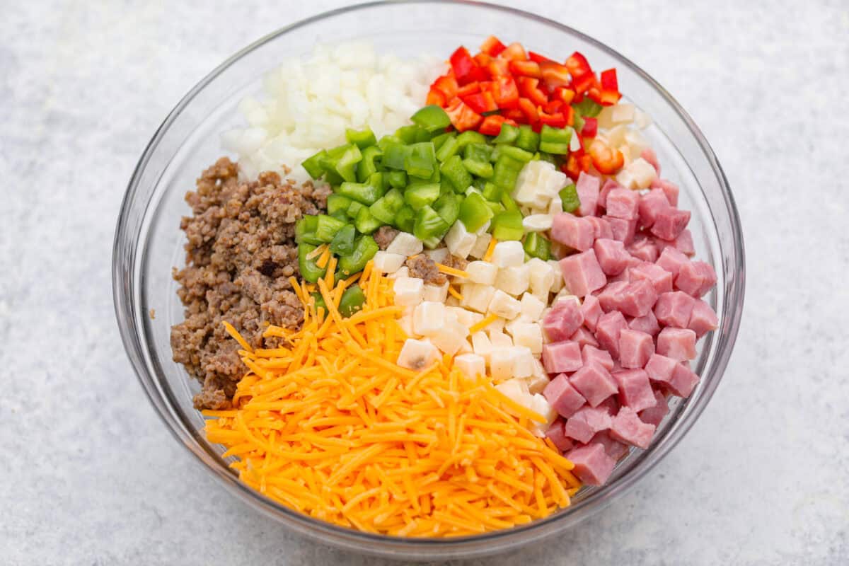 This Slow Cooker Breakfast Casserole is quick and easy to put together! Breakfast can be cooked in the slow cooker while you're sleeping! This casserole is loaded up with seasoned sausage, diced hash browns, tender vegetables, eggs, and cheese. Overhead shot of dived veggies, ham, sausage and cheese in a bowl.