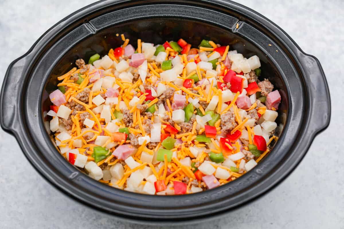 This Slow Cooker Breakfast Casserole is quick and easy to put together! Breakfast can be cooked in the slow cooker while you're sleeping! This casserole is loaded up with seasoned sausage, diced hash browns, tender vegetables, eggs, and cheese. Overhead shot of the ingredients mixed together in the crock pot.