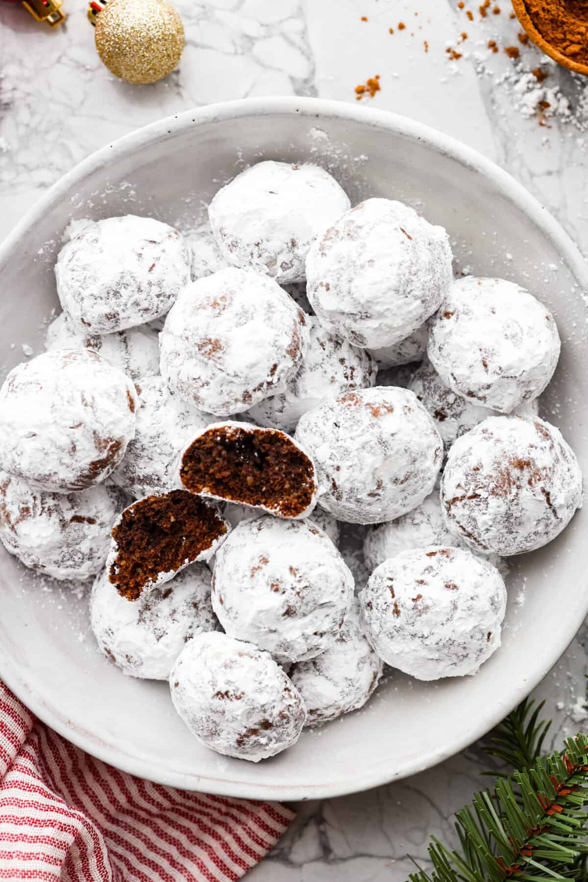 Chocolate Snowball Cookies are tender chocolate cookies with the best texture! A buttery cookie made with cocoa powder and ground walnuts gets coated in sweet powdered sugar. Make this classic holiday cookie a tradition every year! Top view of chocolate snowball cookies in a bowl.