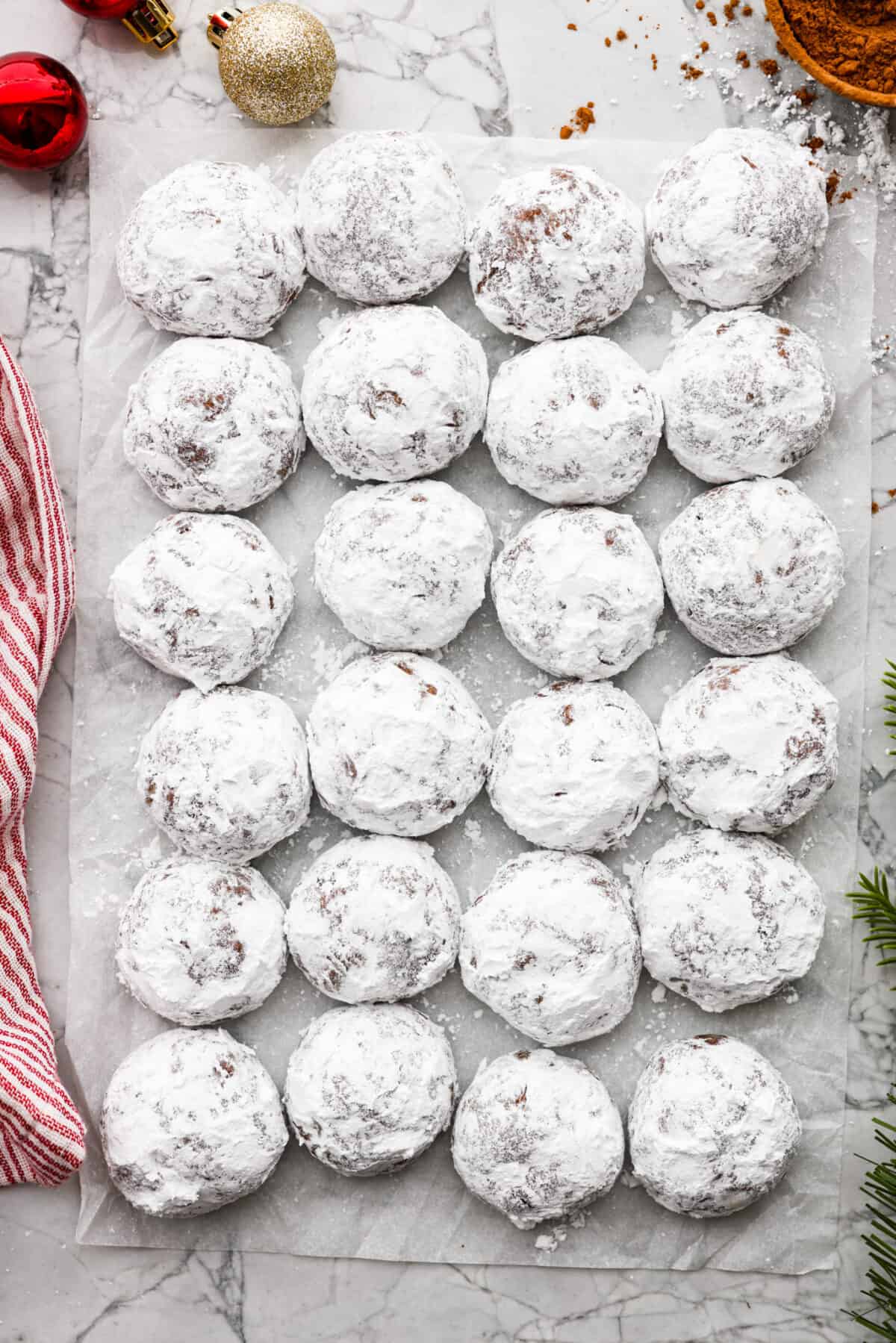 Chocolate Snowball Cookies are tender chocolate cookies with the best texture! A buttery cookie made with cocoa powder and ground walnuts gets coated in sweet powdered sugar. Make this classic holiday cookie a tradition every year! Top view of chocolate snowball cookies lined on parchment paper.