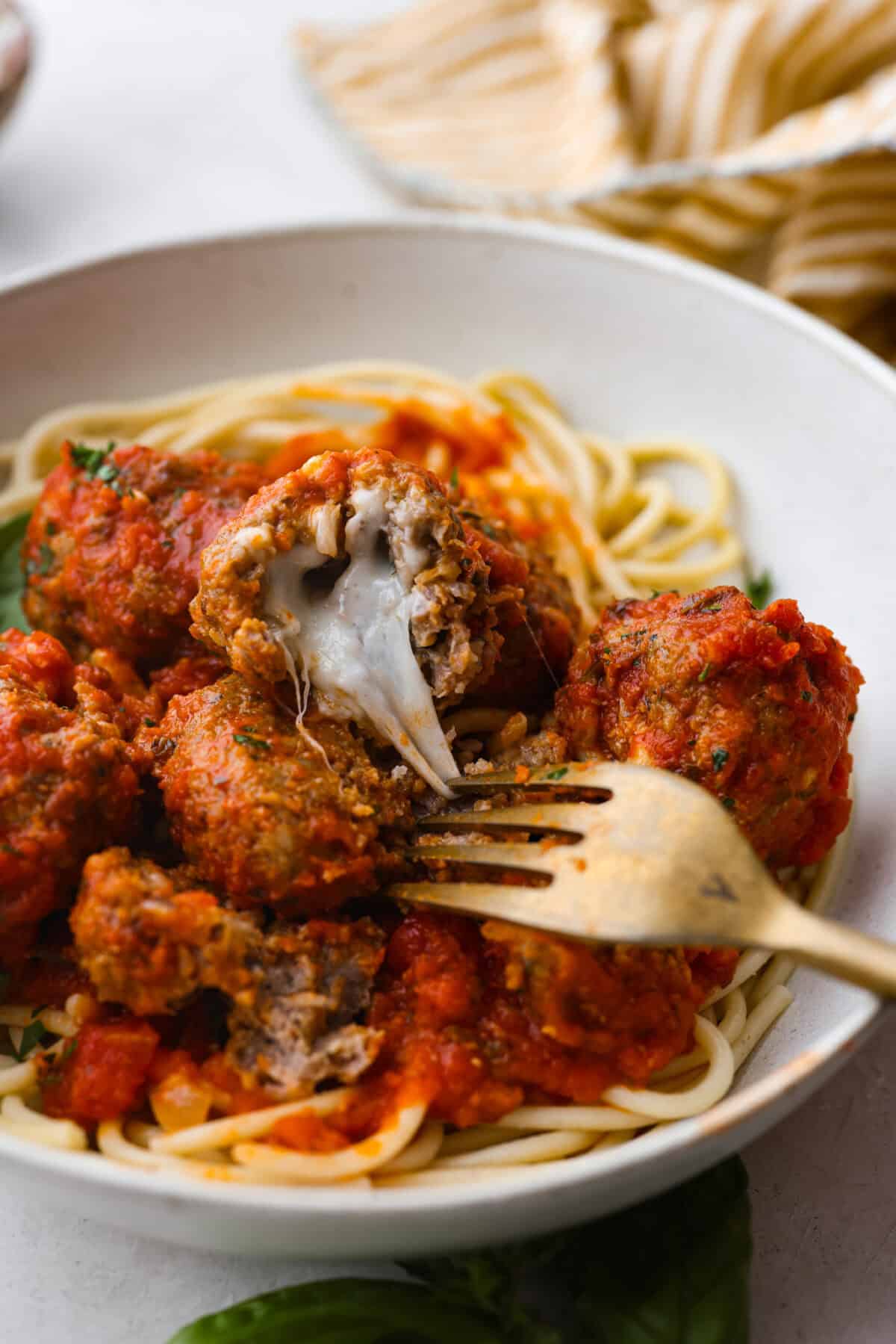Mozzarella Stuffed Meatballs take classic meatballs to the next level! Tender and juicy with melty cheese on the inside. Serve these meatballs as a party appetizer or over spaghetti noodles for a hearty meal! Close view of a fork pulling the melty cheese from a mozzarella stuffed meatball in a bowl.