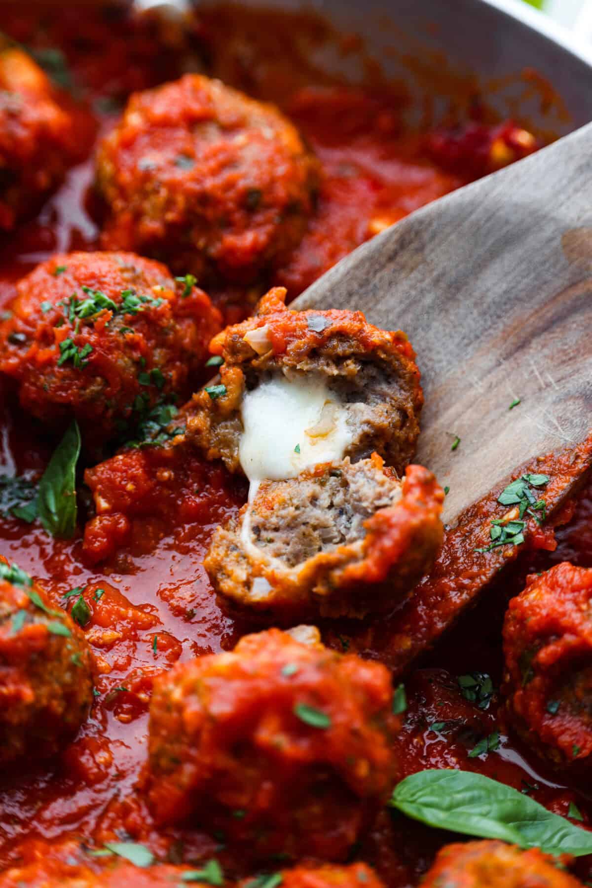 Mozzarella Stuffed Meatballs take classic meatballs to the next level! Tender and juicy with melty cheese on the inside. Serve these meatballs as a party appetizer or over spaghetti noodles for a hearty meal! Close view of a mozzarella stuffed meatballs cut open with melted cheese.