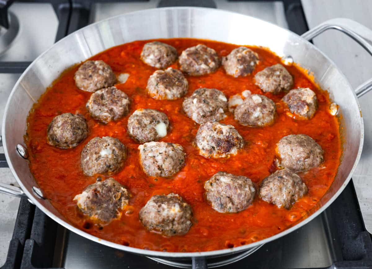 Mozzarella Stuffed Meatballs take classic meatballs to the next level! Tender and juicy with melty cheese on the inside. Serve these meatballs as a party appetizer or over spaghetti noodles for a hearty meal! Sixth photo of the mozzarella stuffed meatballs placed in a pan of marinara sauce.