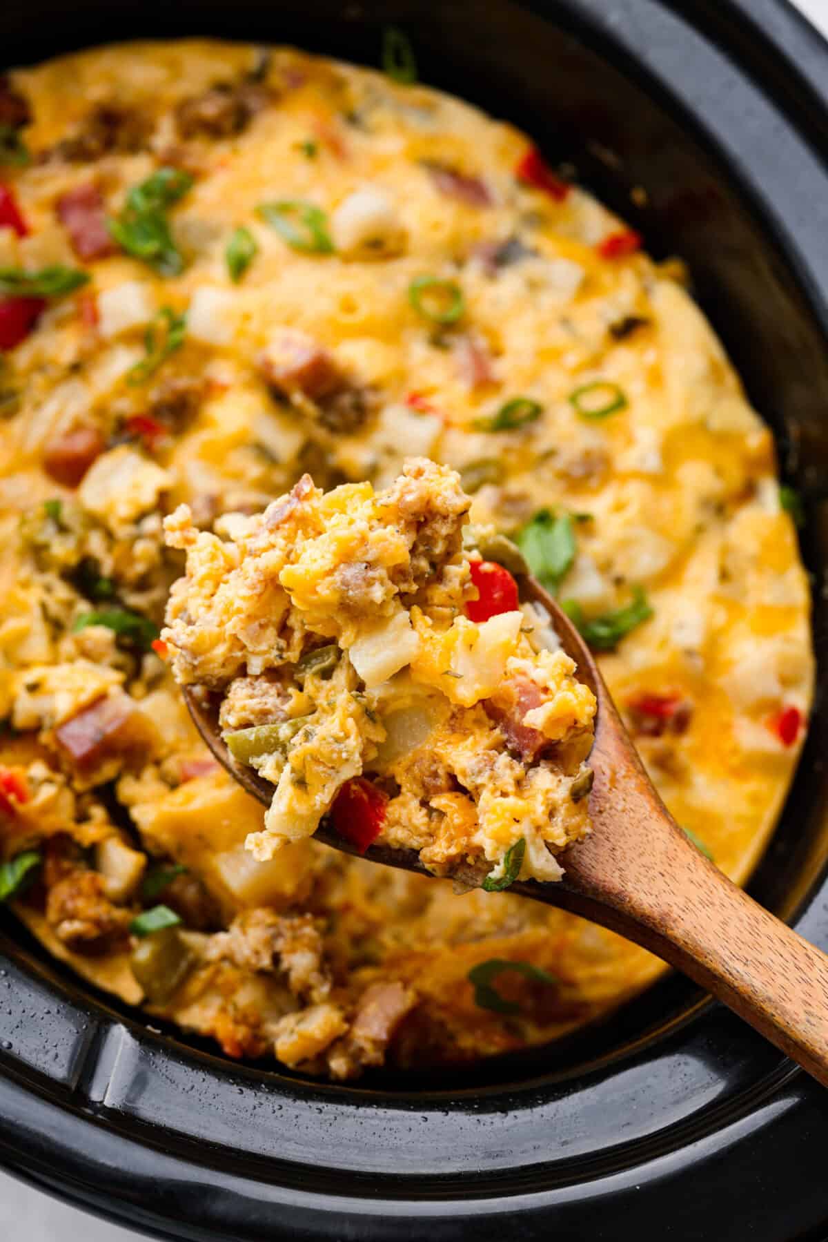 This Slow Cooker Breakfast Casserole is quick and easy to put together! Breakfast can be cooked in the slow cooker while you're sleeping! This casserole is loaded up with seasoned sausage, diced hash browns, tender vegetables, eggs, and cheese. Close up shot of a scoop of slow cooker breakfast casserole on a wooden serving spoon.