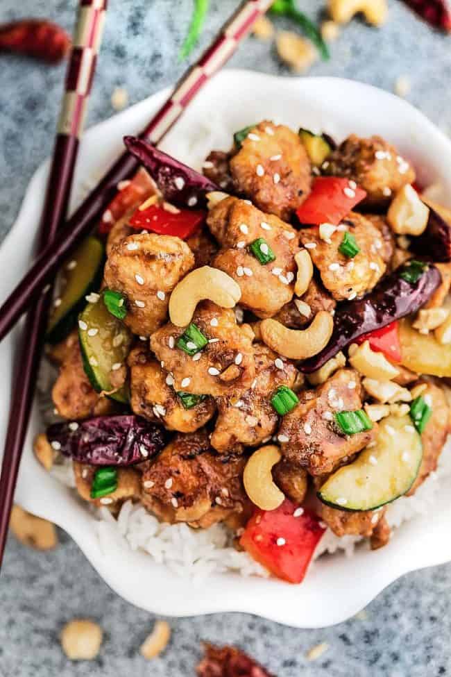 Skinny Slow Cooker Kung Pao Chickenย is aย delicious chicken coated in a sweet and spicy sauce with tender vegetables and crunchyย cashews. Skip the takeout, this is so muchย healthier and better! Skinny Slow Cooker Kung Pao Chicken in a bowl with rice and chopsticks to the side.