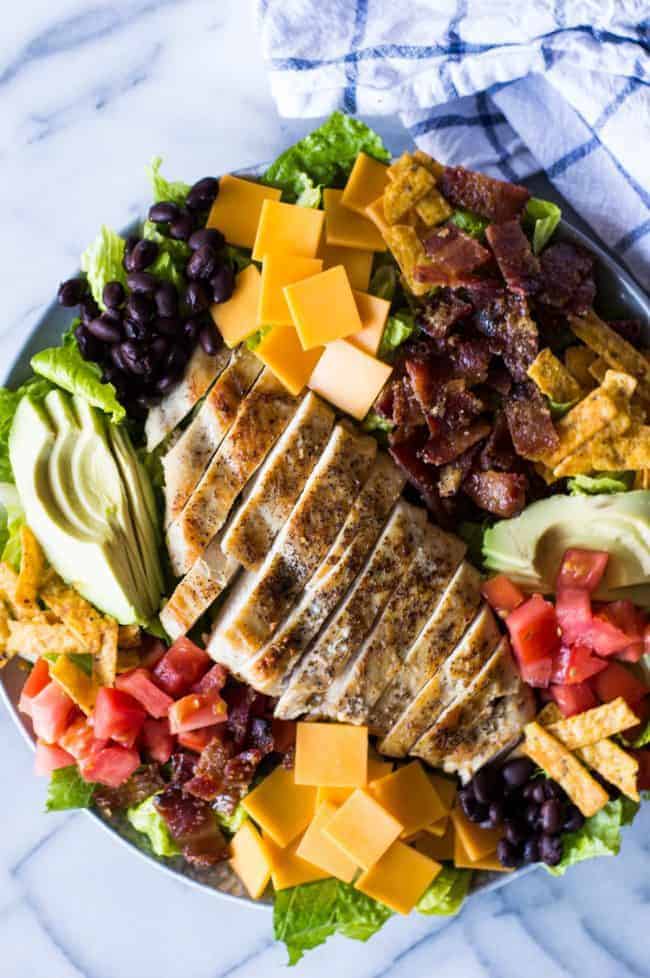 Southwest Grilled Chicken Salad with Candied Bacon. This salad is loaded with grilled chicken, fresh juicy tomato, creamy avocado, crunchy tortilla strips, black beans, cheddar cheese, and sweet and salty candied bacon. All drizzled with a homemade salsa ranch that is truly addicting! Southwest Grilled Chicken Salad with Candied Bacon ingredients.