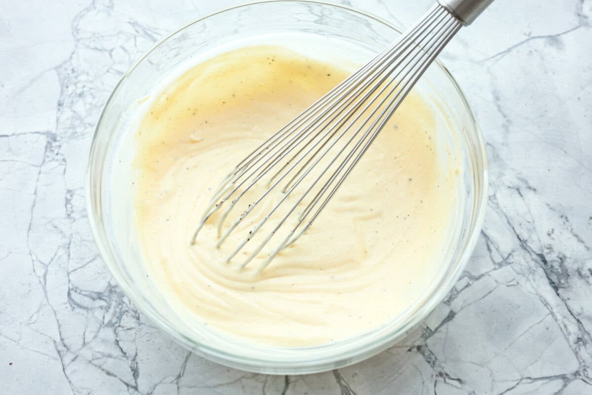 This healthy chicken pasta salad is a fun twist on the classic sandwich recipe. It's filled with penne pasta, tender chunks of chicken breast, crunchy pecans, all tossed in a creamy, sweet dressing. It's the perfect blend of flavors and textures. Overhead shot of bowl dressing with a whisk sticking out.