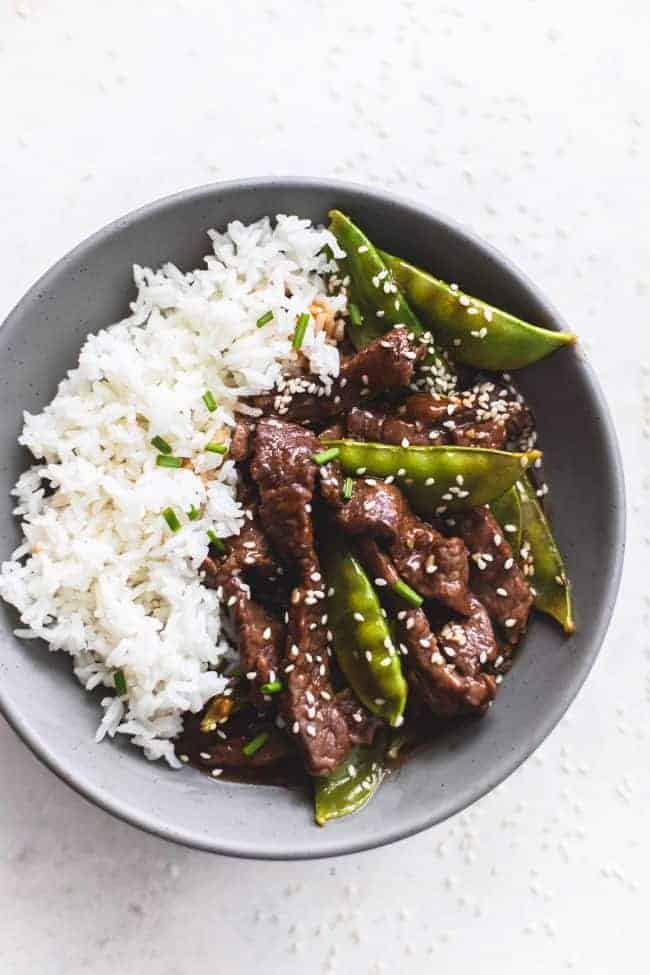 Honey Sesame Beef is a 20 minute meal that is full of amazing flavor! It whips up in 20 minutes and will become your favorite weeknight go to meal! Honey sesame beef on a black plate with white rice.
