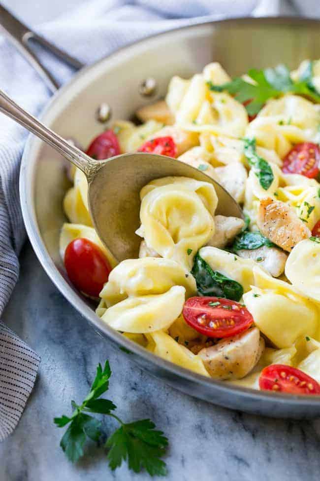 This Oneย Pot Creamy Parmesan Chicken Tortellini is aย family friendly meal that's ready in no time! It's packed full of golden brown chicken, veggies and tortellini, all in a creamy parmesan sauce. Stirring one pot chicken with tortellini.