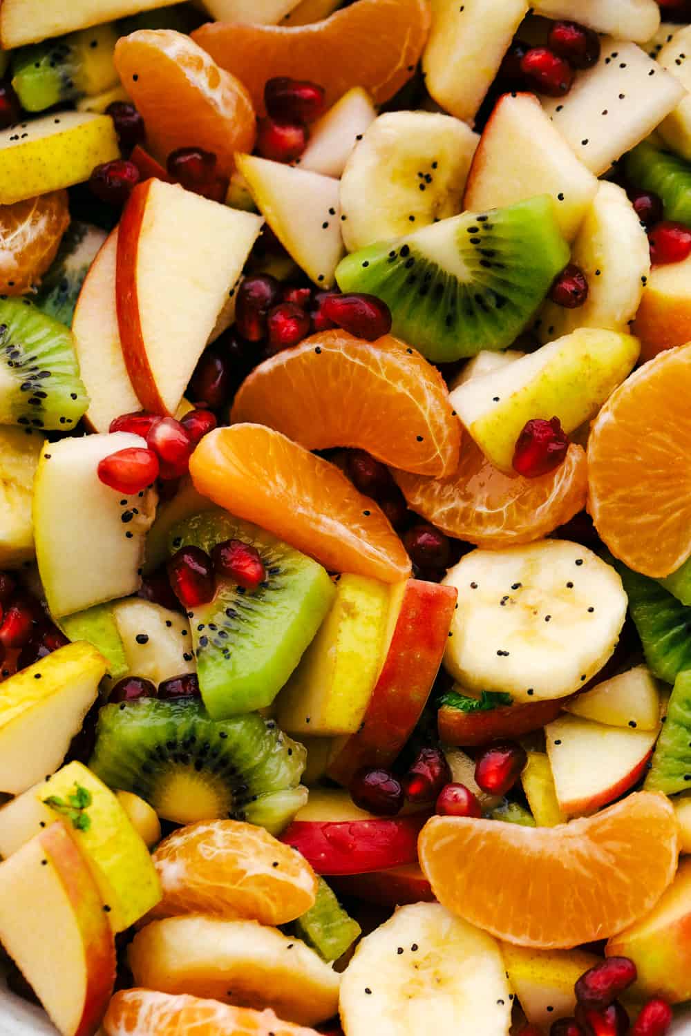 The Best Winter Fruit Salad is filled with clementines, kiwi, pears, apples, and pomegranate, then tossed in sweet tart honey lime poppy seed dressing. These are all fruits that are in season in the fall and winter and when tossed with the most delicious dressing it's a dinner winner for sure. Close up of kiwi, apples, oranges, pomegranates and honey lime dressing.