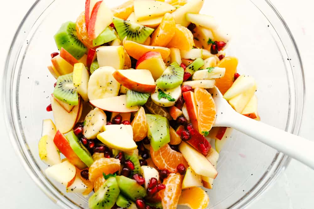 The Best Winter Fruit Salad is filled with clementines, kiwi, pears, apples, and pomegranate, then tossed in sweet tart honey lime poppy seed dressing. These are all fruits that are in season in the fall and winter and when tossed with the most delicious dressing it's a dinner winner for sure. Mixing up the Fruit salad with the poppyseed dressing.