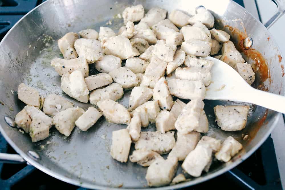 This garlic chicken stir fry is a quick and easy dinner that's perfect for those busy weeknights. Cubes of chicken are cooked with colorful veggies and tossed in a flavorful garlic sauce for a meal that's way better than take out! Stir frying the chicken in the wok.