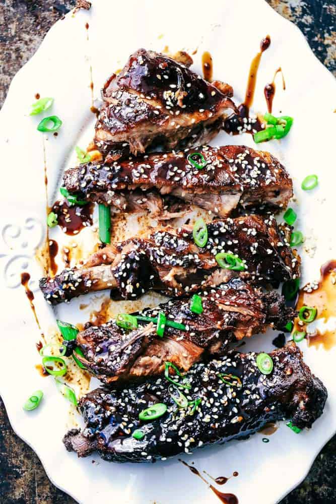 Slow Cooker Sticky Asian Ribs with Sticky Sauce are the very best fall of the bone tender ribs you will ever make! Slow cooked to perfection in a sweet and tangy asian sauce. They get slathered right before serving in a finger licking good sticky sauce! Slow Cooker Sticky Asian Ribs with Sticky Sauce on a white plate.
