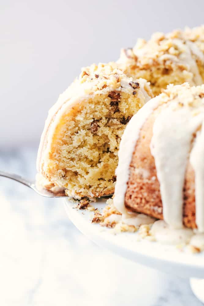 Glazed Walnut Butter Cake is a perfectly moist and tender buttery cake filled with walnuts and made with ingredients you already have on hand. This cake gets a delicious glaze and is topped with chopped walnuts and will become a new favorite! Glazed Walnut Butter Cake with one slice being pulled out.