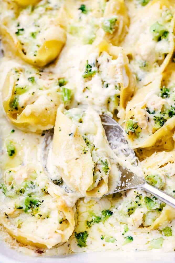 Chicken Broccoli Garlic Alfredo Shellsย are stuffed with tender chicken, cheese, broccoli, and homemade alfredo sauce. These shells are creamy, cheesy and out of this world delicious!ย Chicken Broccoli Garlic Alfredo Shells being scooped up by a large serving spoon.