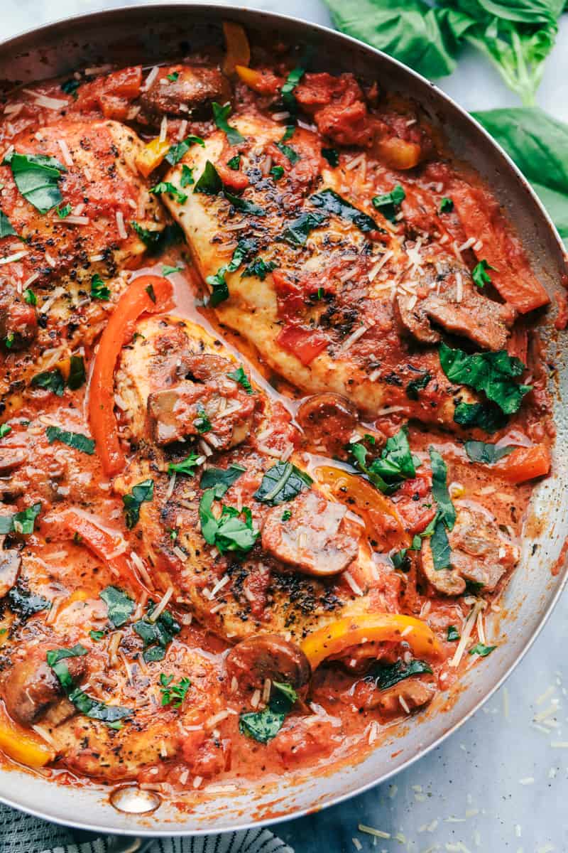 Creamy Skillet Chicken Cacciatore has the most amazing creamy red sauce with peppers, mushrooms, and fresh basil. The chicken is tender and juicy and on the dinner table in 30 minutes!ย Creamy Skillet Chicken Cacciatore close up in skillet.