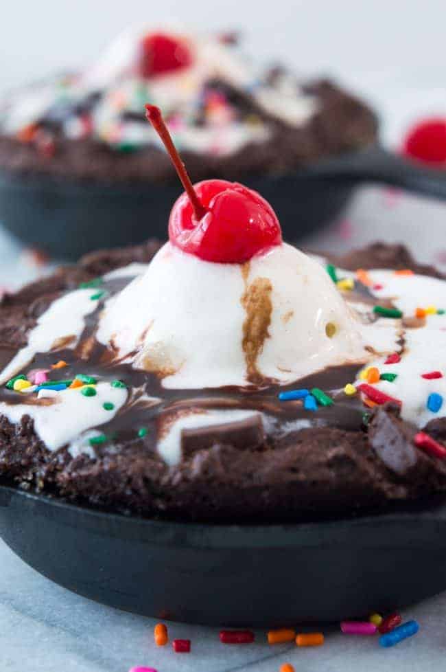 Skillet Brownie Sundaes! ย These mini skillets are filled with warm fudgy brownies loaded with chunks of chocolate and topped with ice cream, chocolate syrup, sprinkles and of course the cherry on top! Perfect small batch dessert for two!ย Skillet Brownie Sundae close up.