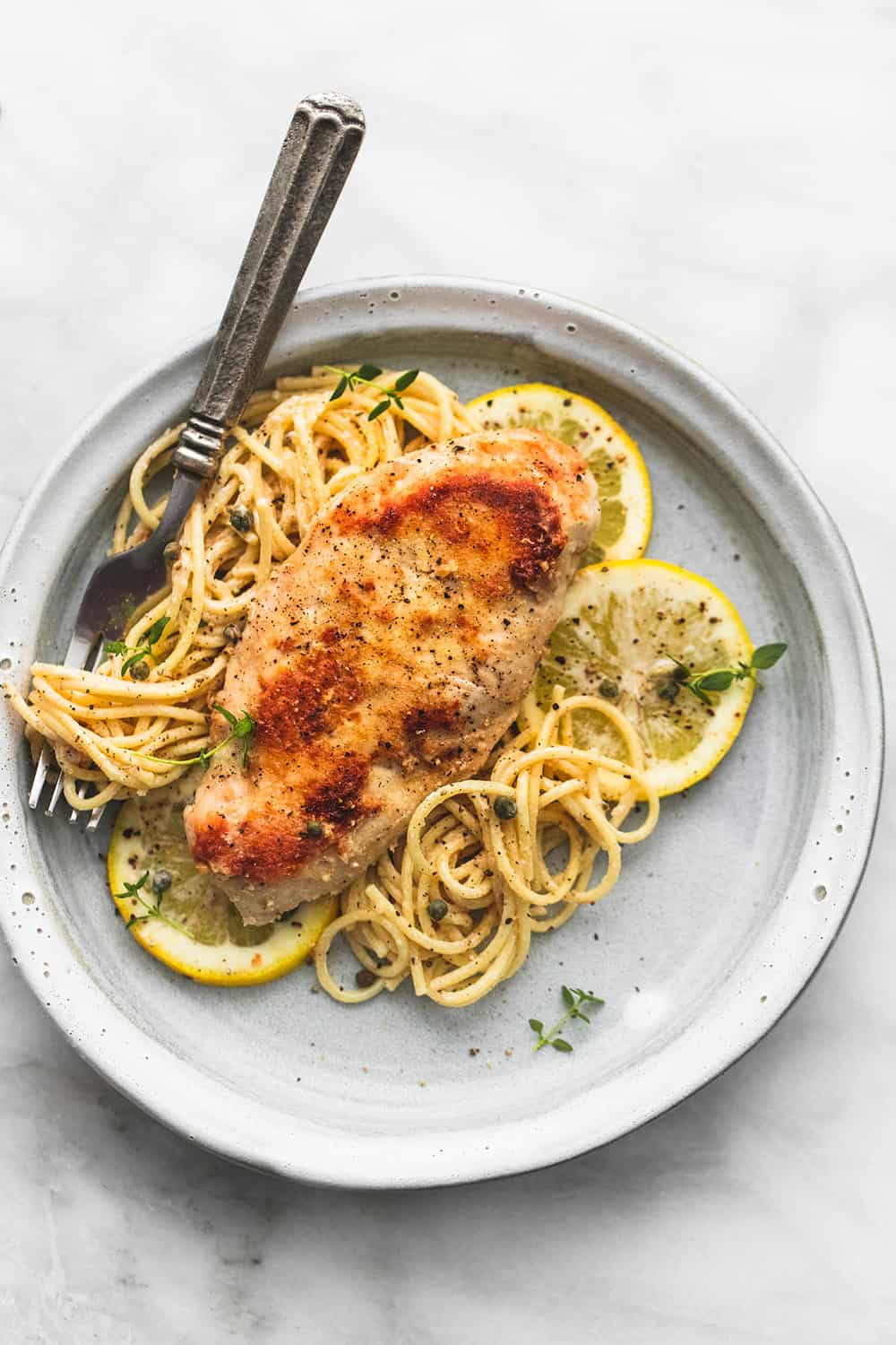 Slow Cooker Lemon Chicken Piccata is creamy lemony sauce-coated noodles with juicy lightly breaded chicken with a hint of garlic, all topped with savory capers! Slow Cooker Lemon Chicken Piccata on a plate with noodles and lemon slices.