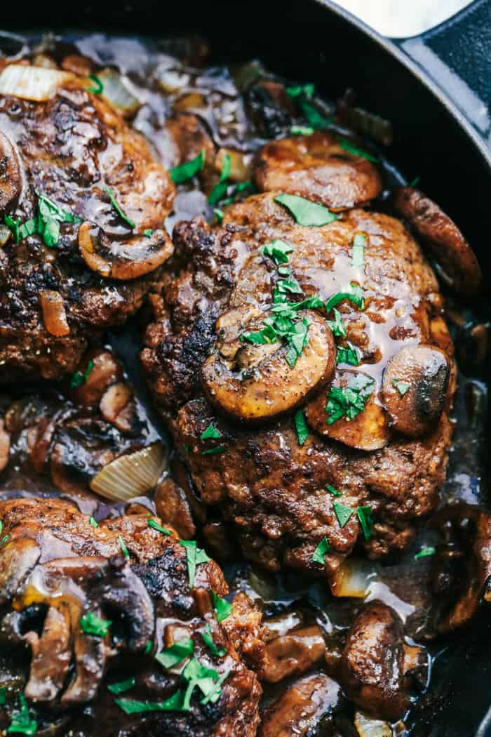 Skillet Salisbury Steak is a classic mealย with a mouthwatering tender beef patty drowning in a rich homemade brown gravy. Serve it over some mashed potatoes and peas and you have yourself a winner! Skillet Salisbury Steak close up in a cast iron pan.