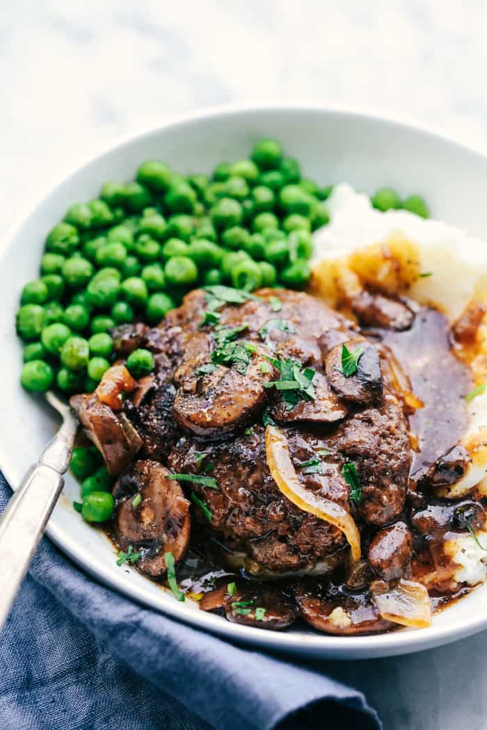 Skillet Salisbury Steak is a classic mealย with a mouthwatering tender beef patty drowning in a rich homemade brown gravy. Serve it over some mashed potatoes and peas and you have yourself a winner! Skillet Salisbury Steak on a white plate with green peas and mashed potatoes.