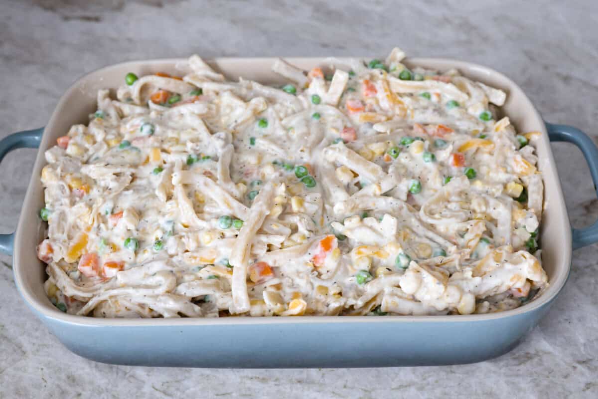 cooked chicken, corn, cream of chicken soup, milk, sour cream, onion flakes, Italian seasoning, garlic powder, salt, pepper, and cheddar cheese. Overhead shot of the casserole mixture spread out in a baking dish.
