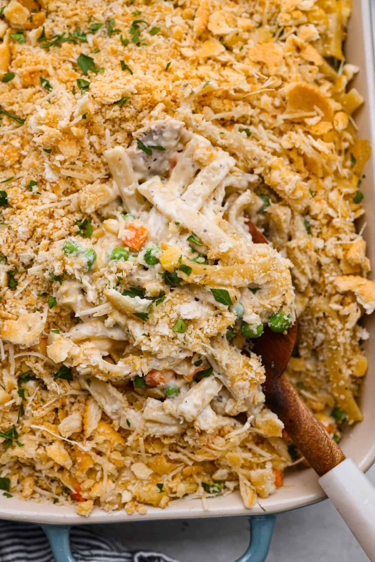 cooked chicken, corn, cream of chicken soup, milk, sour cream, onion flakes, Italian seasoning, garlic powder, salt, pepper, and cheddar cheese. Close up shot of creamy chicken noodle casserole with wooden serving spoon.
