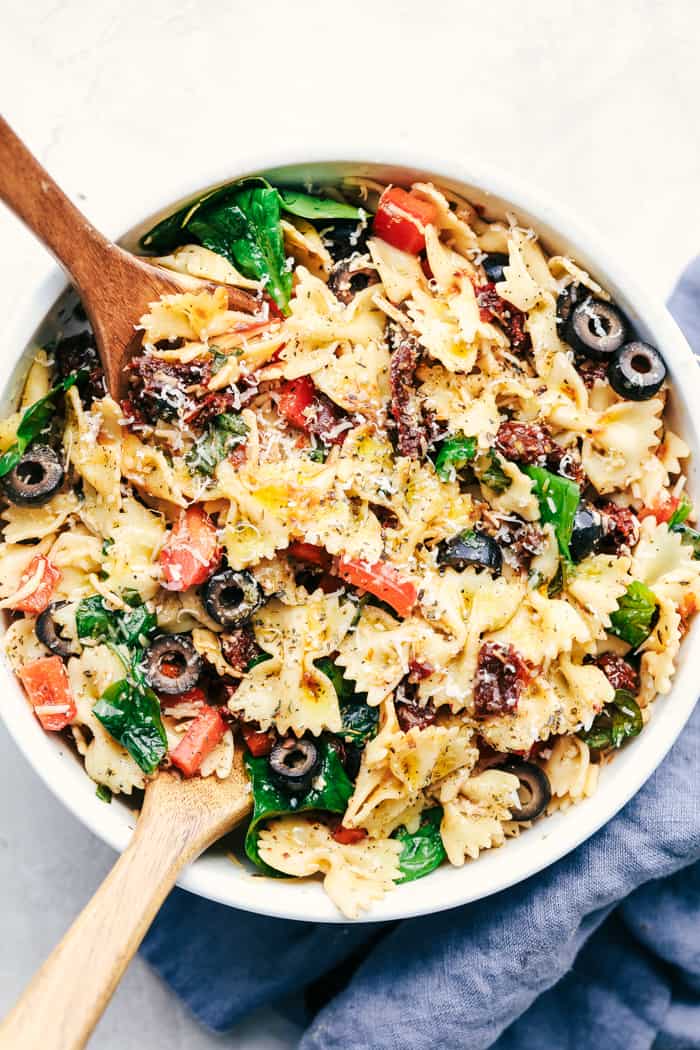 Tuscan Pasta Salad is an easy pasta salad with sun dried tomatoes, peppers spinach, and olives tossed in a tangy dressing. This pasta salad is perfect for your next potluck!ย Tuscan Pasta Salad in a white bowl.