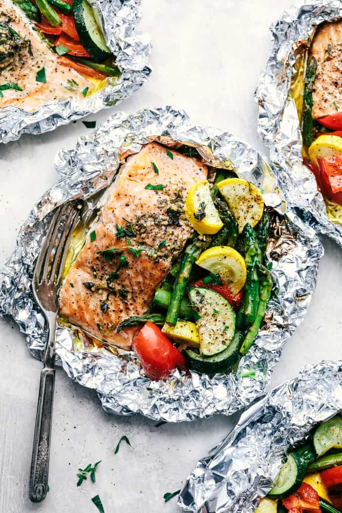 Butter Garlic Herb Salmon Foil Packets are made with tender and flaky salmon with fresh summer veggies. They cook to perfection with the best garlic herb compound and will become a family favorite! Butter Garlic Herb Salmon Foil Packets with a fork.