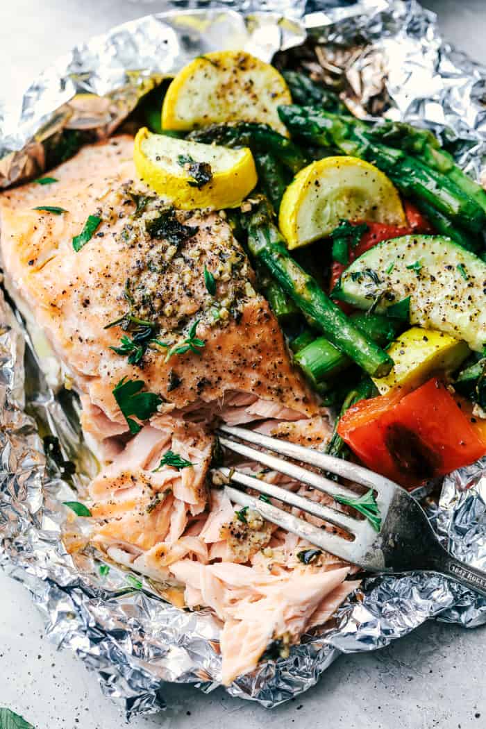 Butter Garlic Herb Salmon Foil Packets are made with tender and flaky salmon with fresh summer veggies. They cook to perfection with the best garlic herb compound and will become a family favorite! Butter Garlic Herb Salmon Foil Packets with a fork pulling the salmon apart.