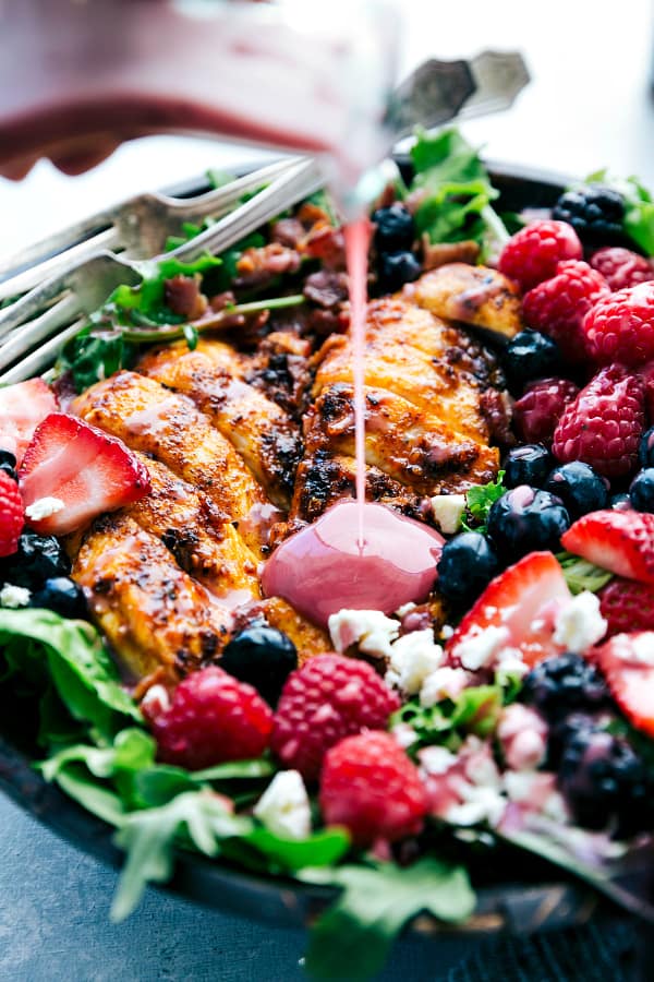 Grilled Berry Feta Chicken Salad is loaded with fresh summer berries, bacon chipotle seasoned grilled chicken and topped with a sweet chipotle dressing! You will be craving this mouthwatering salad all summer long!ย Grilled Berry Feta Chicken Salad with dressing being poured over it.