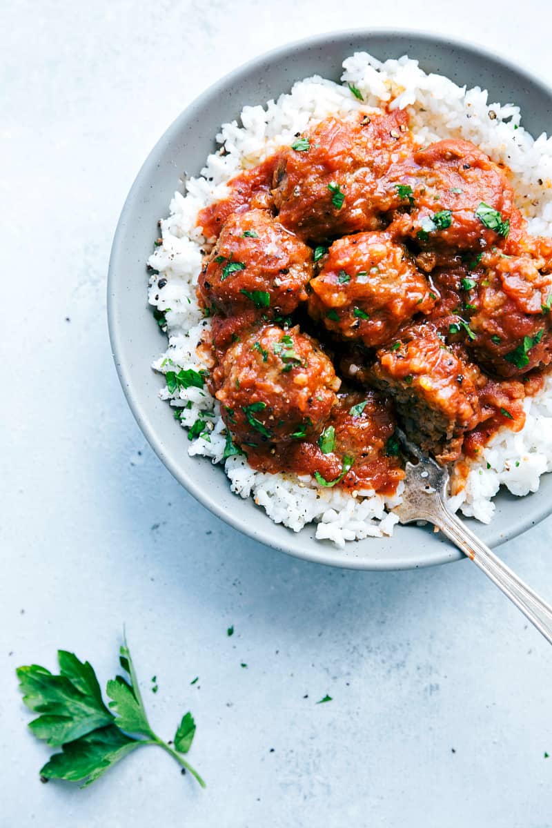 Slow Cooker Porcupine Meatballs are hearty and delicious meatballs filled with rice and served with a rich tomato sauce. This is a classic meal that the family will love!!ย Slow Cooker Porcupine Meatballs on rice in a gray bowl.