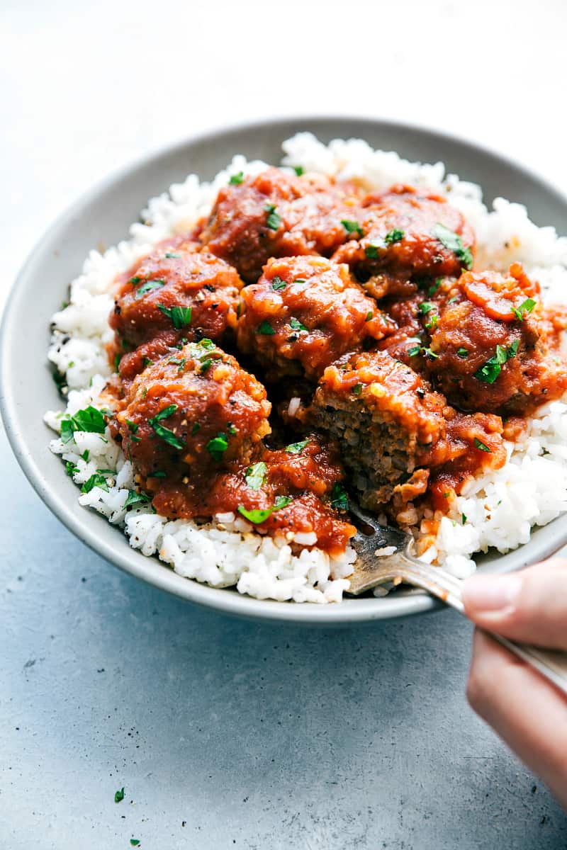 Slow Cooker Porcupine Meatballs are hearty and delicious meatballs filled with rice and served with a rich tomato sauce. This is a classic meal that the family will love!!ย Slow Cooker Porcupine Meatballs on white rice and a gray bowl.
