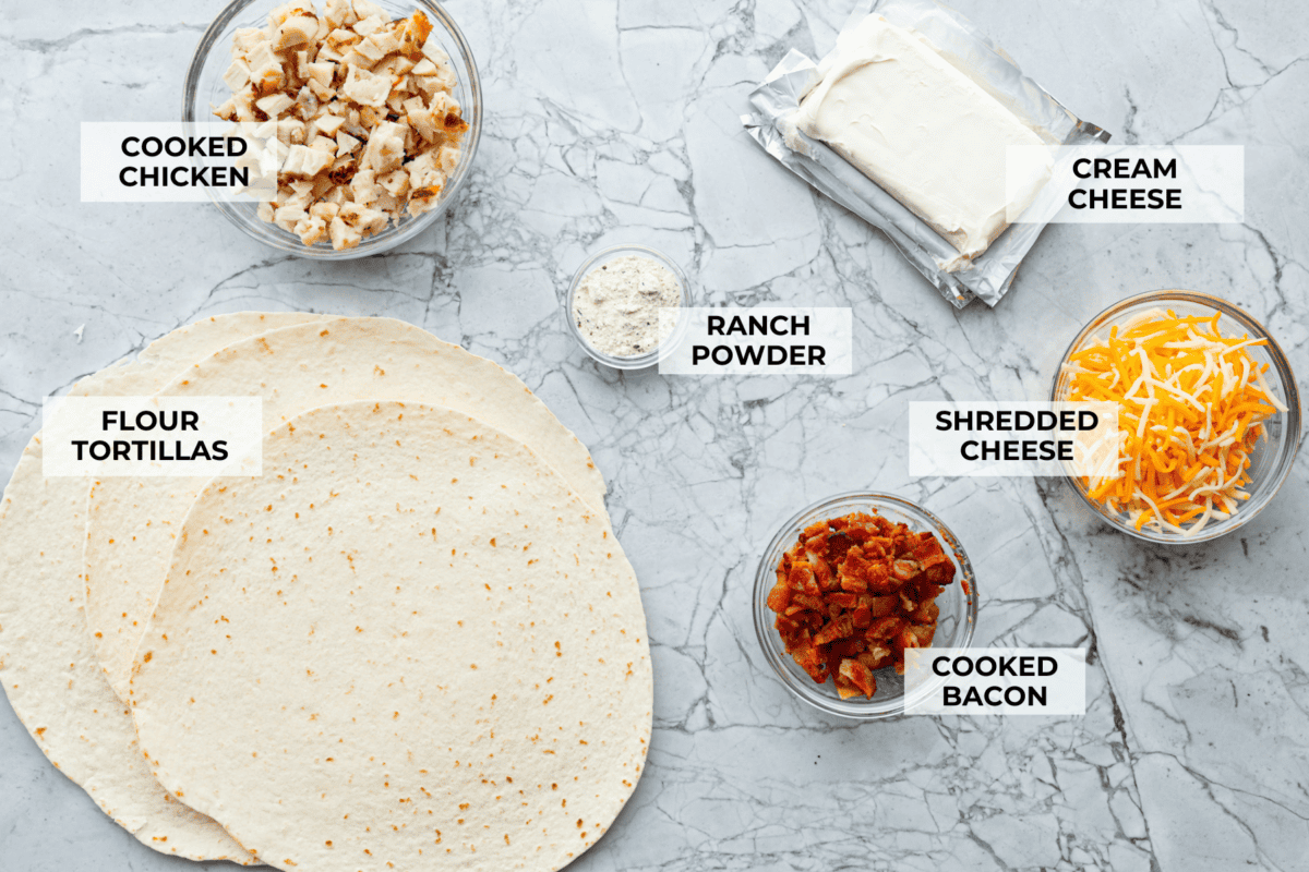 Chicken Bacon Ranch Pinwheels are an easy wrap your family or party guests will love! They are rolled up and loaded with hearty chicken, savory bacon, and cheese, all slathered in a delicious ranch-flavored cream cheese. You can enjoy them both hot and cold! Overhead shot of labeled ingredients.