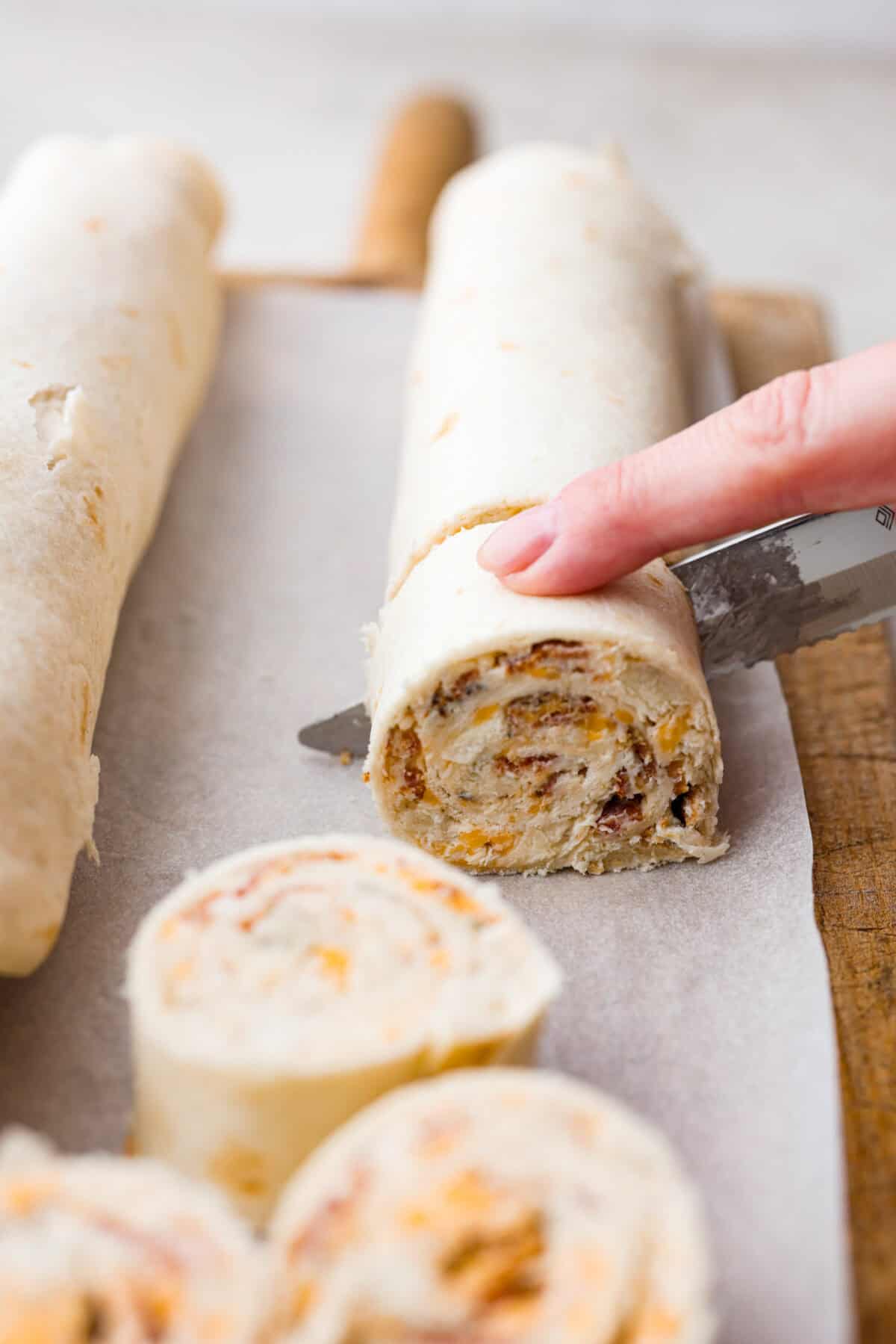 Chicken Bacon Ranch Pinwheels are an easy wrap your family or party guests will love! They are rolled up and loaded with hearty chicken, savory bacon, and cheese, all slathered in a delicious ranch-flavored cream cheese. You can enjoy them both hot and cold! Close up shot of someone cutting the pinwheel into one inch slices.