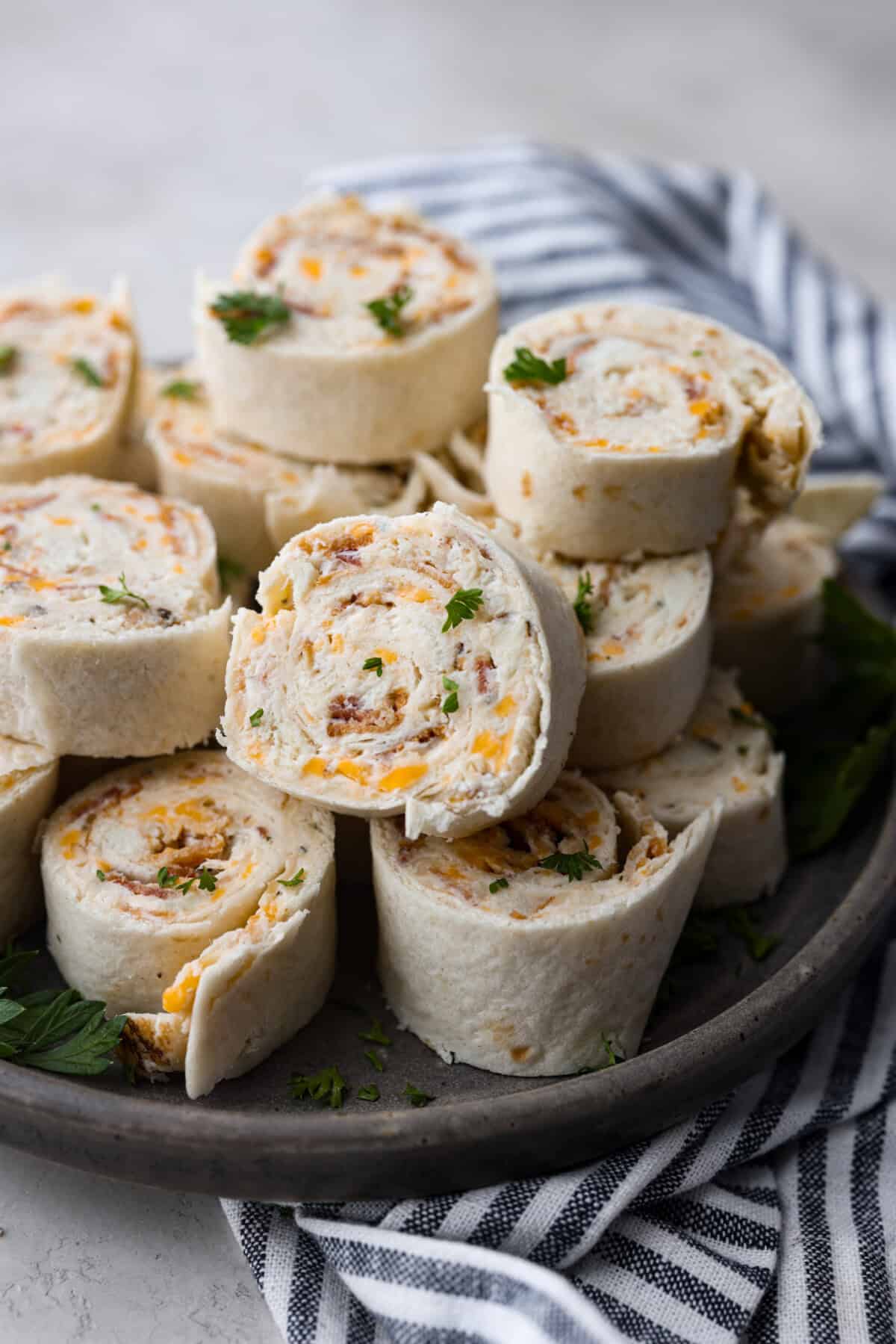 Chicken Bacon Ranch Pinwheels are an easy wrap your family or party guests will love! They are rolled up and loaded with hearty chicken, savory bacon, and cheese, all slathered in a delicious ranch-flavored cream cheese. You can enjoy them both hot and cold! Side shot of stacked chicken bacon ranch pinwheels.