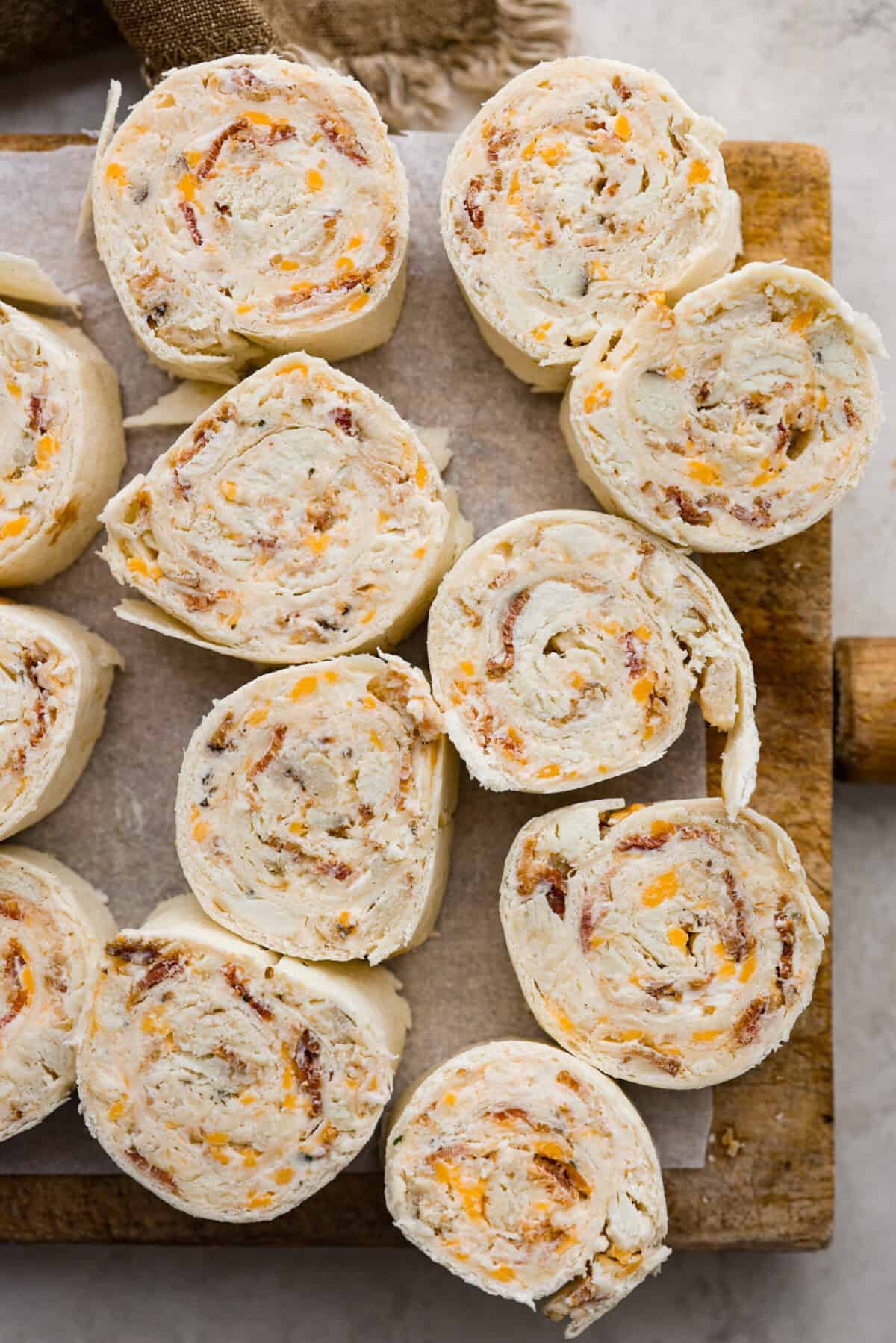 Chicken Bacon Ranch Pinwheels are an easy wrap your family or party guests will love! They are rolled up and loaded with hearty chicken, savory bacon, and cheese, all slathered in a delicious ranch-flavored cream cheese. You can enjoy them both hot and cold! Overhead shot of chicken bacon ranch pinwheels on a wooden cutting board.