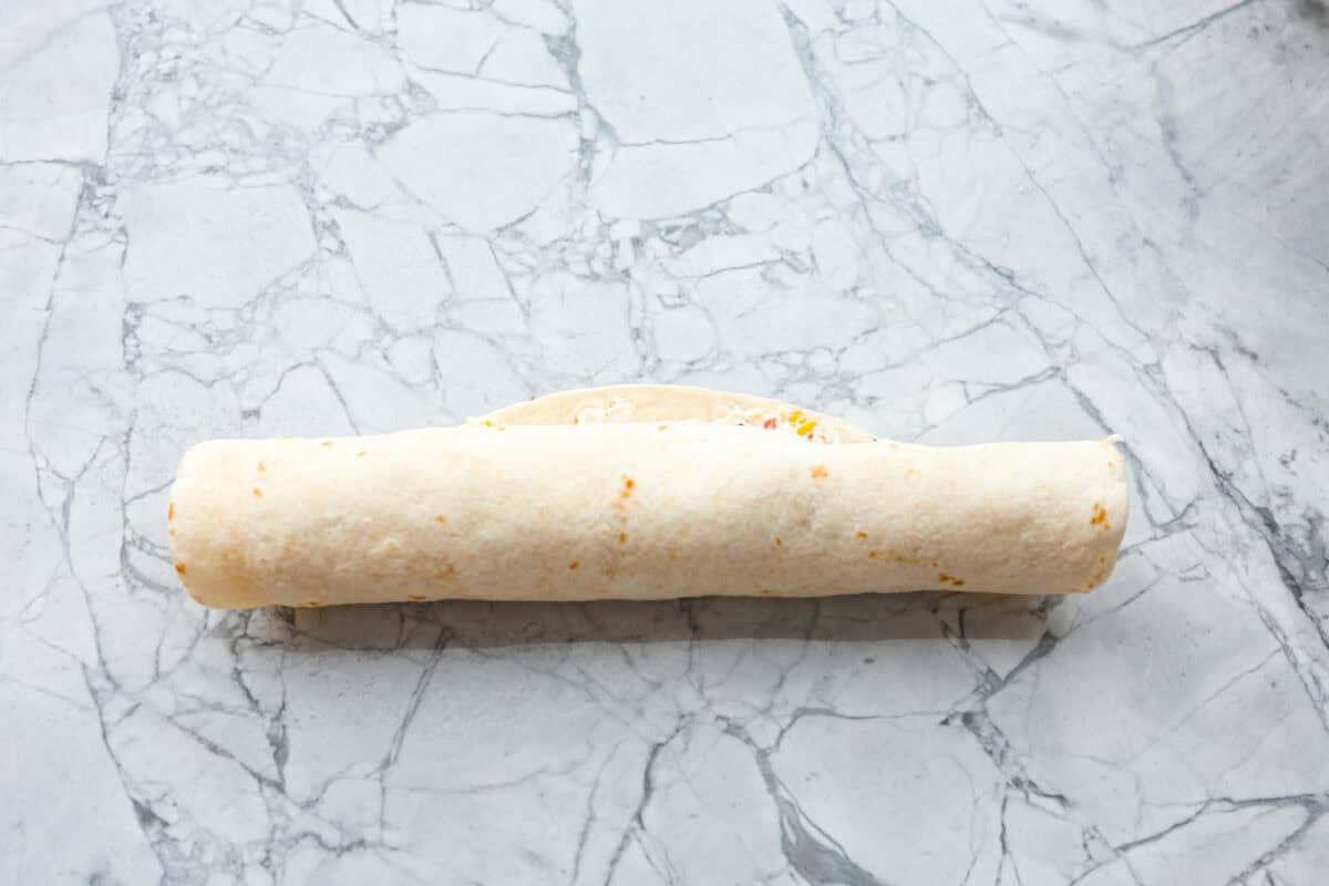 Chicken Bacon Ranch Pinwheels are an easy wrap your family or party guests will love! They are rolled up and loaded with hearty chicken, savory bacon, and cheese, all slathered in a delicious ranch-flavored cream cheese. You can enjoy them both hot and cold! Overhead shot of rolled up tortilla with filling.