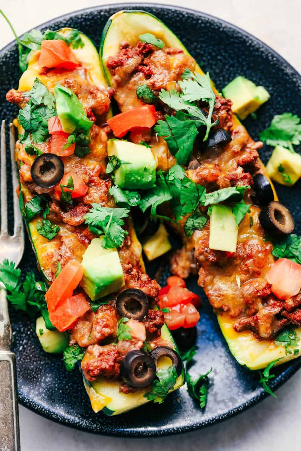Taco Stuffed Zucchini Boats are loaded with taco seasoned ground beef, cheese and topped with your favorite toppings. These make a delicious low carb meal and are perfect for using up that zucchini! Taco Stuffed Zucchini Boats on plate