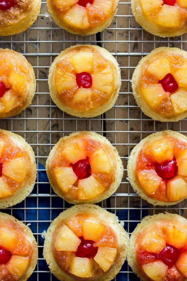 Sweet and simple pineapple upside down-cupcakes made entirely from scratch (donโt worry, theyโre easy!). With fluffy vanilla cupcake bases topped off with caramelized pineapple and maraschino cherries, these are a great new way to enjoy a classic recipe! Easy, from-scratch, pineapple upside-down cupcakes on a cooling rack in rows.