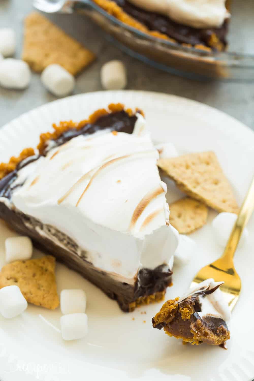 This No Bake S'mores Pie is the easiest summer dessert! A graham cracker crust is loaded with chocolate filling and topped with marshmallow cream! Slice of No Bake S'mores Pie on a white plate.