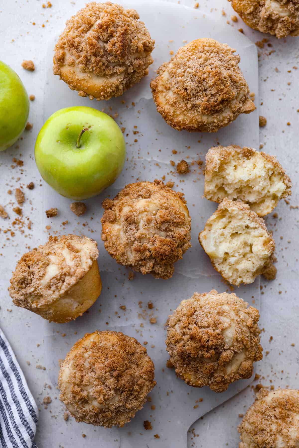 Apple Crumb Muffins are sweet and fluffy bakery-style muffins topped with a brown sugar crumble.ย Every bite is loaded with fresh apple pieces and spiced to perfection! Top close view of apple crumb muffins on a marble slab with a muffin broken torn in half.